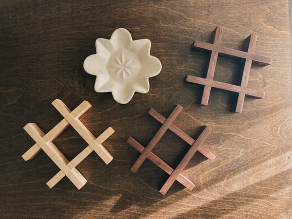 Three grid-shaped wooden trivets laying flat alongside a cream colored star-shaped ceramic dish.